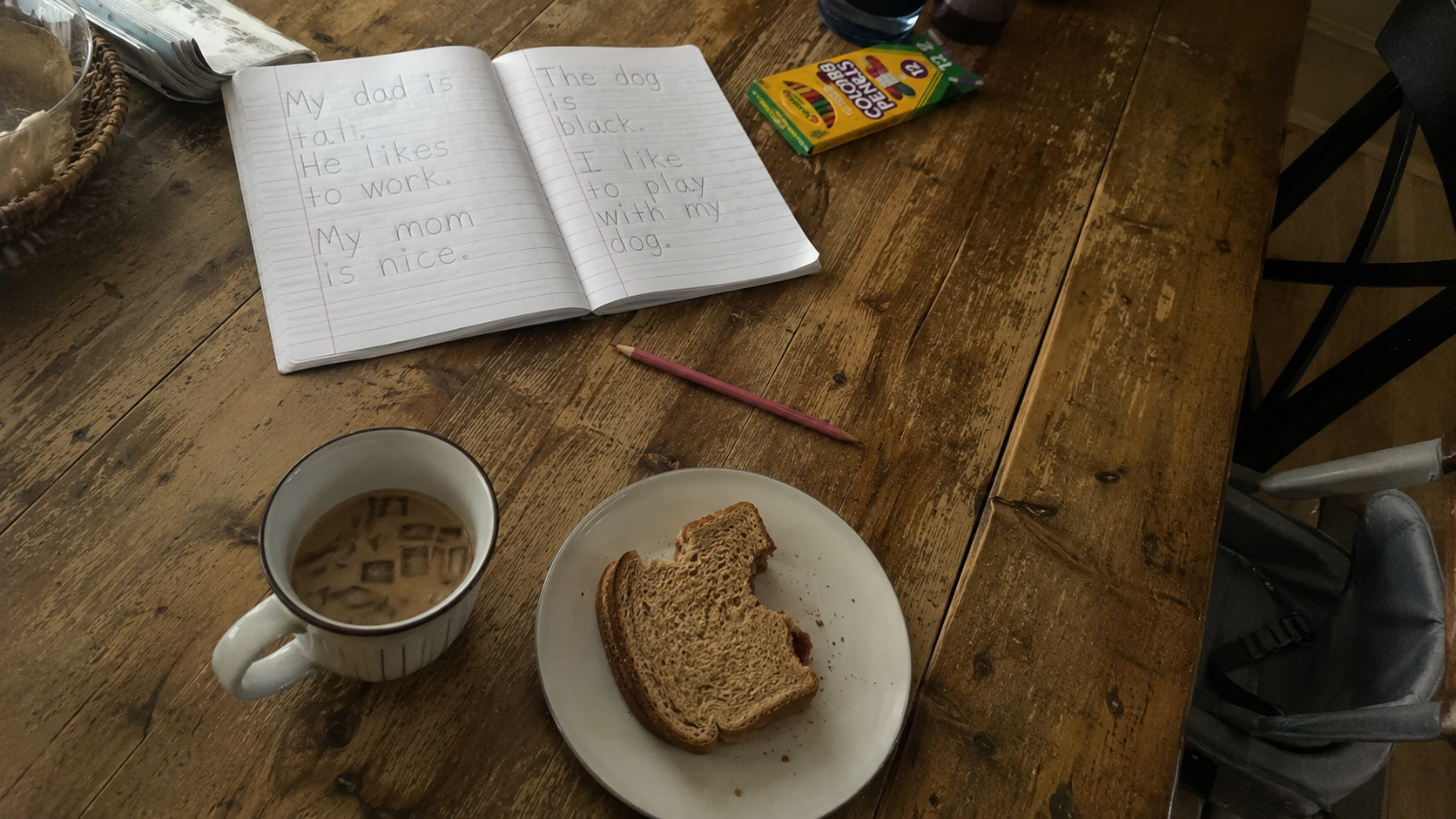 A candid snapshot of a messy wooden dining table featuring a child's notebook, pencil, and a snack, capturing the everyday reality of raising a cooperative learner.
